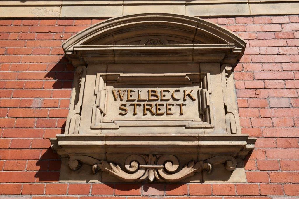 Carved stone Welbeck Street sign on a red-brick facade
